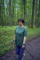 mayor mujer es comprometido en nórdico caminando con palos en el primavera bosque foto