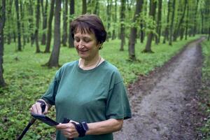 mayor mujer haciendo nórdico caminando con palos en primavera bosque interruptores podcast en teléfono foto