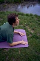 old woman practices yoga in the morning on the river bank, came from home by bicycle photo