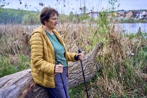 elderly woman rests on the river bank after Nordic walking exercise photo