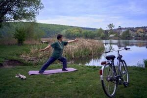 antiguo mujer practicas yoga en el Mañana en el río banco, llegó desde hogar por bicicleta foto