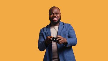 Joyous BIPOC gamer celebrating after winning gaming console game, studio background. Delighted man bragging after being victorious in game, defeating all enemies using gamepad, camera B video