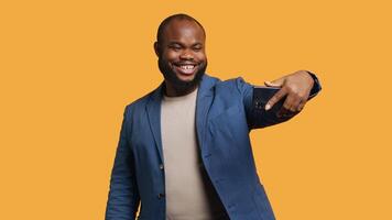 Joyous man using smartphone to take selfies and post them on social media. Happy BIPOC person taking photos using phone selfie camera, isolated over yellow studio background, camera A video