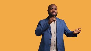 Portrait of african american lecturer holding monologue using microphone, gesturing with hands, studio background. Expressive BIPOC speaker talking during presentation using mic, camera B video