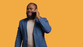 Joyous man with positive emotion, enjoying talking with friends phone call using smartphone, studio background. Happy african american person with smile on face during telephone call, camera A video