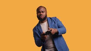 Portrait of cheerful BIPOC man playing games holding controller, studio background. Gamer smiling, having fun by participating in PvP online multiplayer game using console system, camera B video