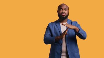 Portrait of assertive BIPOC man asking for timeout, doing hand gestures, feeling fatigued. Unhappy person doing vehement pause sign gesturing, wishing for break, studio background, camera B video