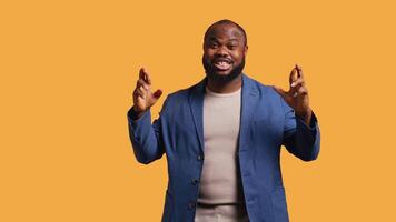 Portrait of upbeat african american man crossing fingers, making wish, isolated over yellow studio background. Jolly BIPOC person hoping for good luck, waiting for miracle, camera B video