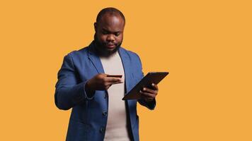 irriterad man upprörd efter saknas pengar medan påfrestande till köpa grejer uppkopplad. vresig person ser på debitera kort efter få transaktion avvisade på läsplatta, håller på med ansiktspalm, studio bakgrund, kamera b video