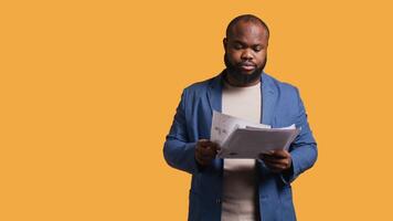 Accountant doing profit analysis for company, feeling perplexed by confusing data, studio background. Worker doing financial budgeting, scratching head, puzzled by financial figures, camera B video