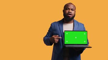 vrolijk Afrikaanse Amerikaans Mens Holding groen scherm laptop, aan het doen aanbeveling. vriendelijk bipoc persoon richten naar mockup notitieboekje, geven positief feedback, studio achtergrond, camera b video