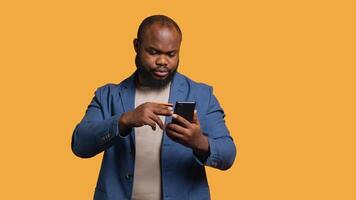 Lycklig man tillsats betalning metod på telefon hemsida, förtjust till ta fördel av kampanjer, studio bakgrund. person glada till do internet handla, skriver kreditera kort data på smartphone, kamera en video