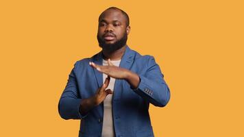 Portrait of assertive BIPOC man asking for timeout, doing hand gestures, feeling fatigued. Unhappy person doing vehement pause sign gesturing, wishing for break, studio background, camera A video