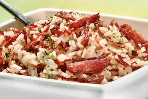 Arroz de Carreteiro, a classic Brazilian dish with rice, dried meat, sliced bacon, onion and parsley photo