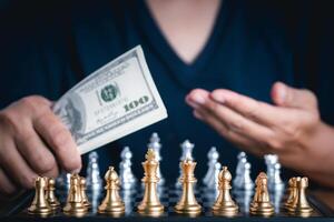 Front view of a chess game with blur background. Close-up of a young man hand holding dollar currency playing chess. Business game competitive strategy. Concept of strategy for business photo