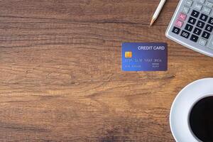 Top view of a blue credit card, pencil, calculator, coffee cup on wooden table in the office. Space for text. Wood texture background. Business and finance concept photo