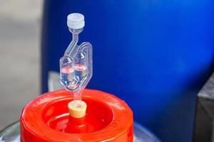 Close-up of a bubbling airlock on fermentation container. Rubber Stopper for a glass carboy. Process of making home beer from malt. Craft beer from barley and dark malt photo