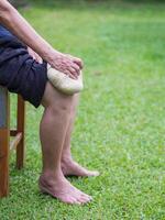 Knee pain in a senior person. Senior woman having knee pain use Thai herbal compress ball on a knee to reduce knee. Knee pain may cause by muscle strain, tendinosis, osteoarthritis photo