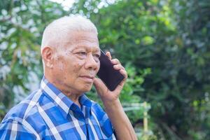 Portrait of an elderly Asian man using a smartphone while standing in a garden. Space for text. Concept of aged people and communication photo