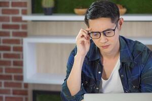 Young businessman looking at a laptop and very worried about a new project while sitting in the office. Space for text. Concept of business photo