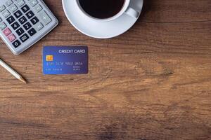 Top view of a blue credit card, pencil, calculator, coffee cup on wooden table in the office. Space for text. Wood texture background. Business and finance concept photo