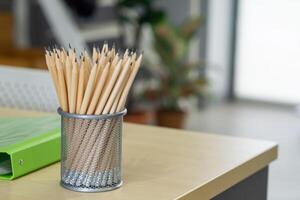 Close-up of many pencils are in the mesh box and placed on the desk work, besides there are a green document file and the computer. Desk Office in the workplace photo