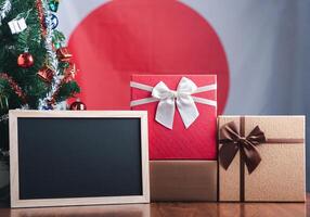 pequeño pizarra y regalo cajas en de madera mesa con un Navidad árbol y Japón bandera en el antecedentes. espacio para texto. concepto de Navidad y nuevo año festival foto