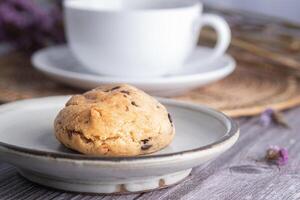 Close-up of a cookie on a plate with a white coffee cup and flower blurred background. Space for text photo