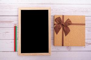 Top view of small blackboard, pencil and brown gift box with a brown ribbon on white wooden table. Space for text. Concept of the anniversary, Christmas, and more festivals photo