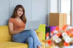 Asian businesswoman is an e-commerce entrepreneur sitting on a chair, smile, and are chatting with customers through a laptop in her office. Young woman's wearing casual cloth. Business Concept photo