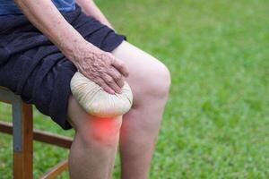 Knee pain in a senior person. Senior woman having knee pain use Thai herbal compress ball on a knee to reduce knee. Knee pain may cause by muscle strain, tendinosis, osteoarthritis photo