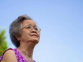 Senior woman wearing glasses, smiling, and looking up while standing in a garden. Space for text. Concept of aged people and healthcare photo