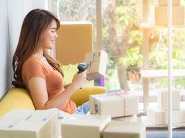 Asian businesswoman is an e-commerce entrepreneur sitting on a chair, smile, with the right hand holding the barcode reader and the left hand holding the parcel box. Concept of business photo