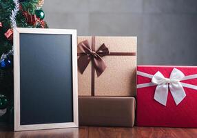 Small blackboard and gift boxes on wooden table with a Christmas tree and vintage wall background. Space for text. Concept of Christmas and new year festival photo