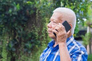 Senior man using a smartphone while standing in a garden. Space for text. Concept of aged people and technology photo