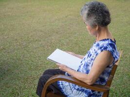 mayor mujer sentado leyendo un libro a el silla en el jardín. espacio para texto. concepto de Envejecido personas y relajación foto