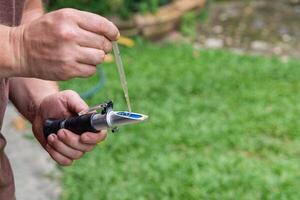 Close-up of hands young man holding refractometer for measure craft beer sugar level. Selective focus. Home brewing process photo