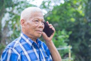Senior man using a smartphone while standing in a garden. Space for text. Concept of aged people and technology photo