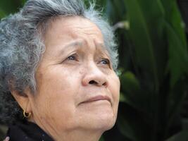 Senior Asian woman with short white hair smiling and looking away while standing in a garden. Space for text. Concept of aged people and healthcare photo