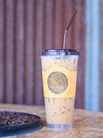 Iced coffee cup placed on a wooden table near the coffee beans in the cafe shop. Space for text. Concept of beverage photo