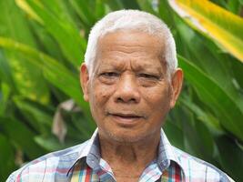 Portrait of an elderly Asian man smiling and looking at the camera while standing in a garden. Concept of aged people and healthcare photo