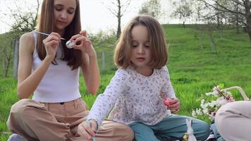 een familie van drie meisjes van verschillend leeftijden en Europese uiterlijk zijn zittend in de tuin Aan de groen gras en zijn verloofd in schilderij Pasen eieren. Pasen tradities. voorjaar vakantie. video