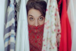 Happy woman shopper in red dress peeking through clothes rack. photo