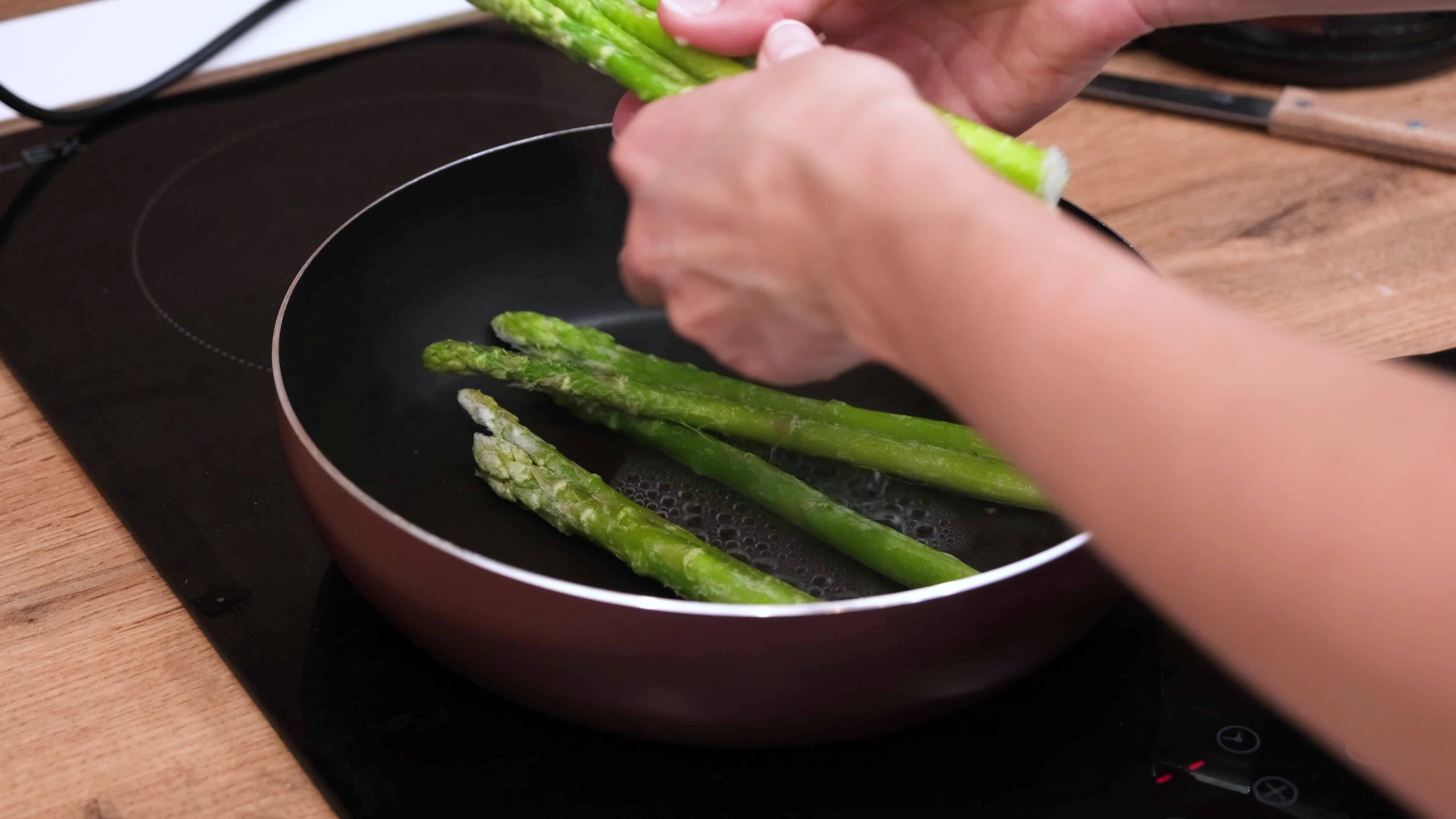 Healthy food woman cooking fresh asparagus in a pan in the kitchen