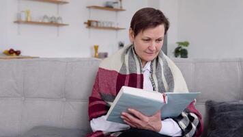 senior vrouw lezing een boek terwijl zittend Aan de bankstel Bij huis. pensioen levensstijl van vrouw zelf isoleren in quarantaine vergrendeling video