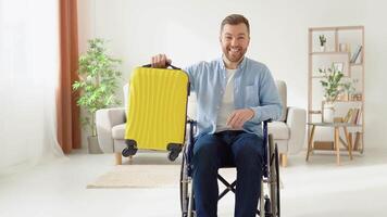 Happy disabled person in a wheelchair with a yellow suitcase in his hands is preparing for a trip video