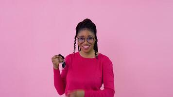 Cute cheerful young african american girl holding a car key. Teen girl housewife beginner standing on a solid pink background video