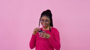 schattig vrolijk jong Afrikaanse Amerikaans meisje in roze kleren houdt de sleutel naar de auto en zet het in een speelgoed- boodschappen doen mand. tiener meisje huisvrouw beginner staand Aan een solide roze achtergrond video