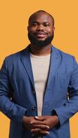Vertical Portrait of cheerful african american man smiling, looking pleased, isolated over yellow studio background. Happy expressive BIPOC person stylishly dressed grinning, feeling satisfied, camera B video