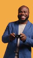 Vertical Upset man showing thumbs down sign gesturing holding controller, disapproving of games. Displeased BIPOC person against gaming, doing rejection hand gesture, studio background, camera B video